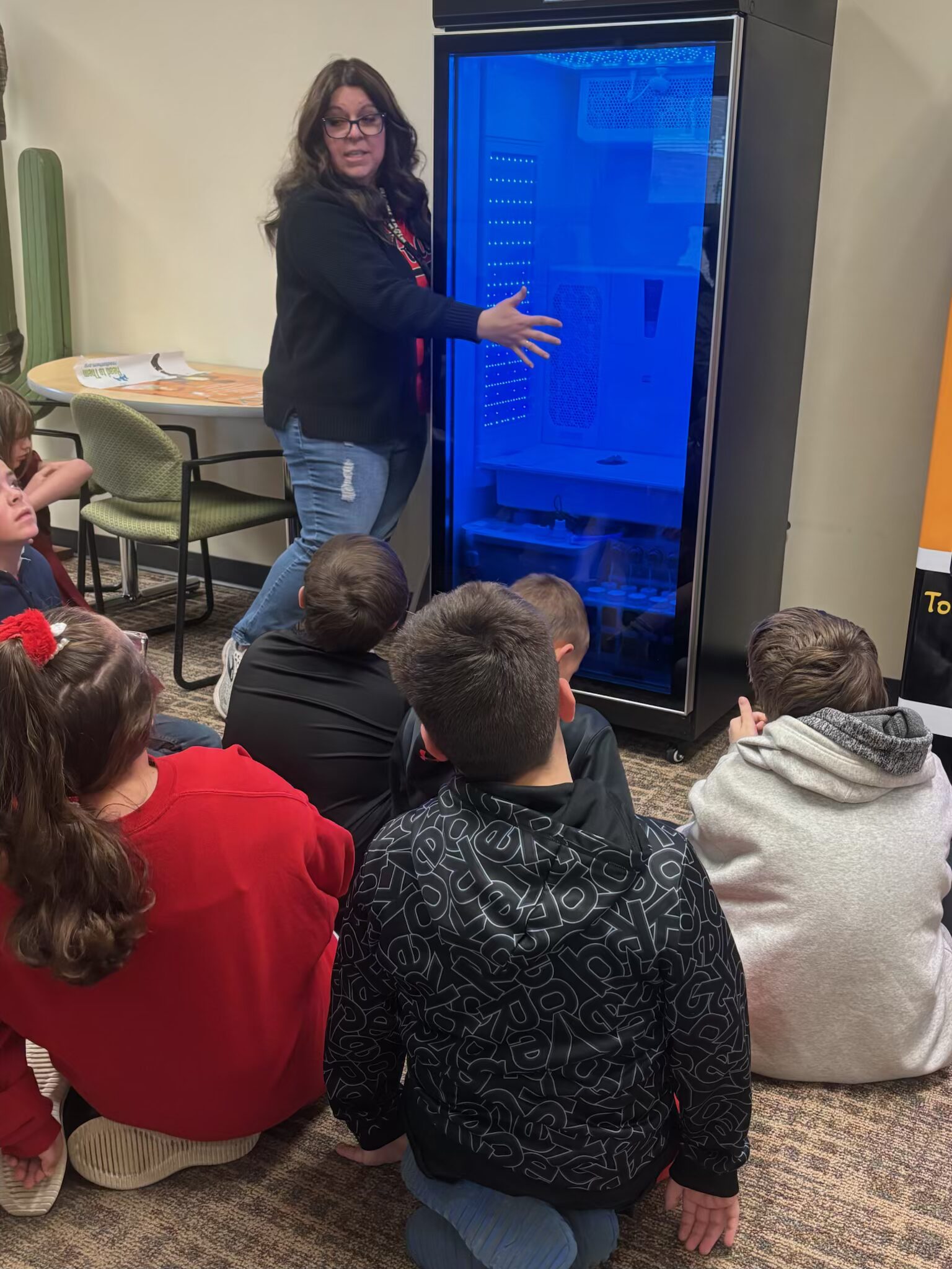 "A teacher demonstrating the interior of a hydroponic growth chamber to young students."